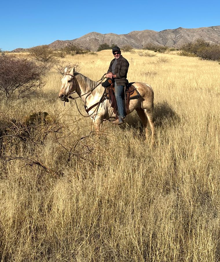Craig on horseback in tall golden grass, the Dragoon Mountains behind him